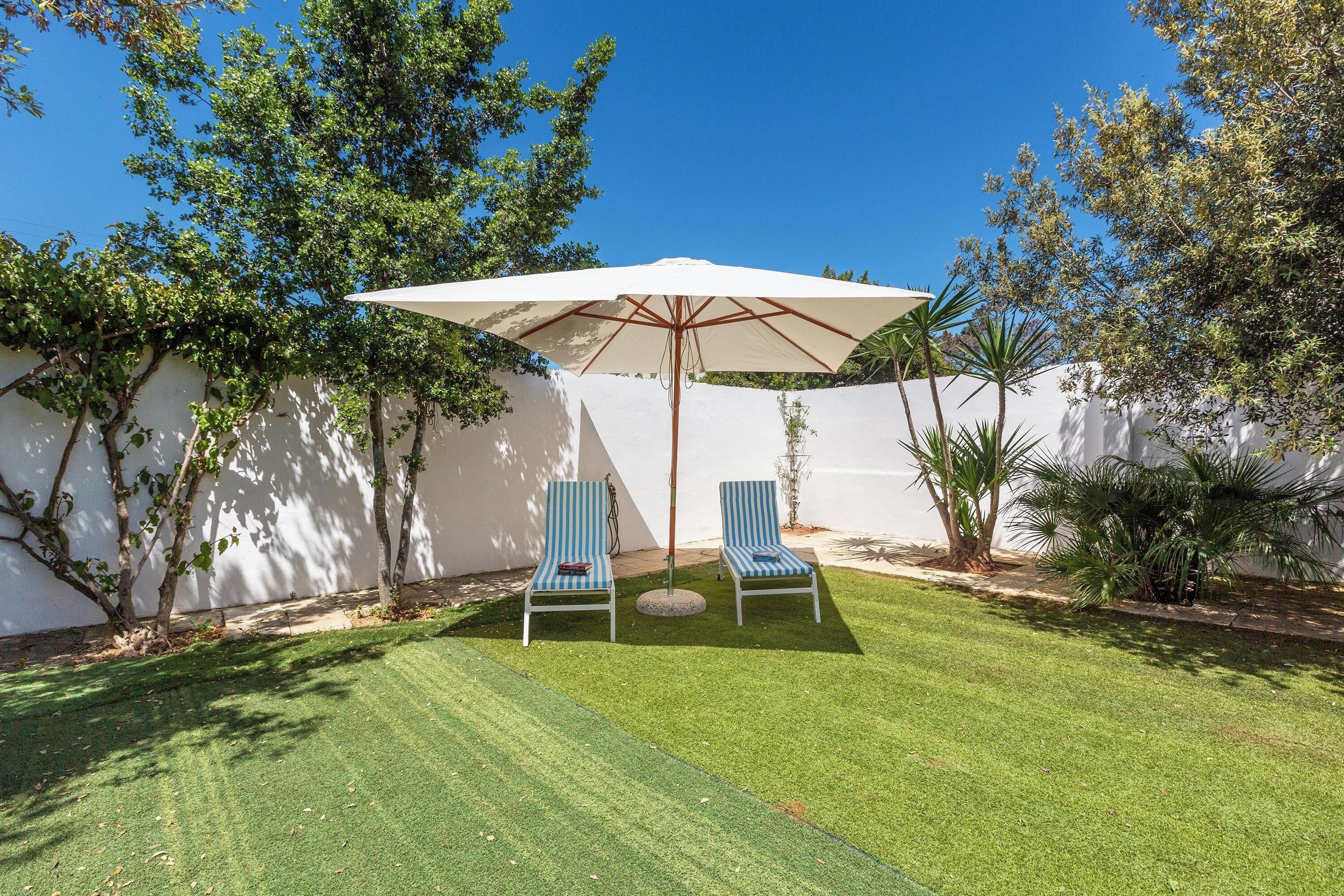 A backyard with two blue lounge chairs, a white umbrella, and a well-maintained lawn.