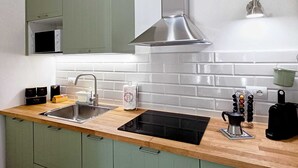 A modern kitchen with green cabinets, a stainless steel range hood, a double sink, and a microwave.