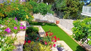 A well-maintained garden with various plants and flowers, a stone wall, and a clear blue sky.