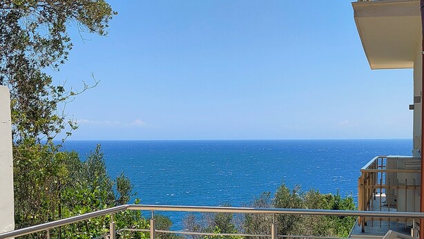 A balcony with a view of the sea, a table, and two lounge chairs.