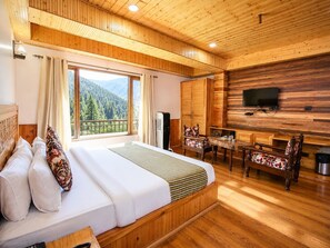 A wooden cabin with a bed, a dining table, chairs, a TV, and a view of the mountains. - The Hillside Kasol (Bhuntar)
