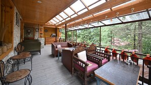 L’intérieur est en bois et une grande baie vitrée donne sur une forêt. On y trouve des bancs et des tables en bois, ainsi qu’un mur de pierre sur lequel sont accrochées des corbeilles.