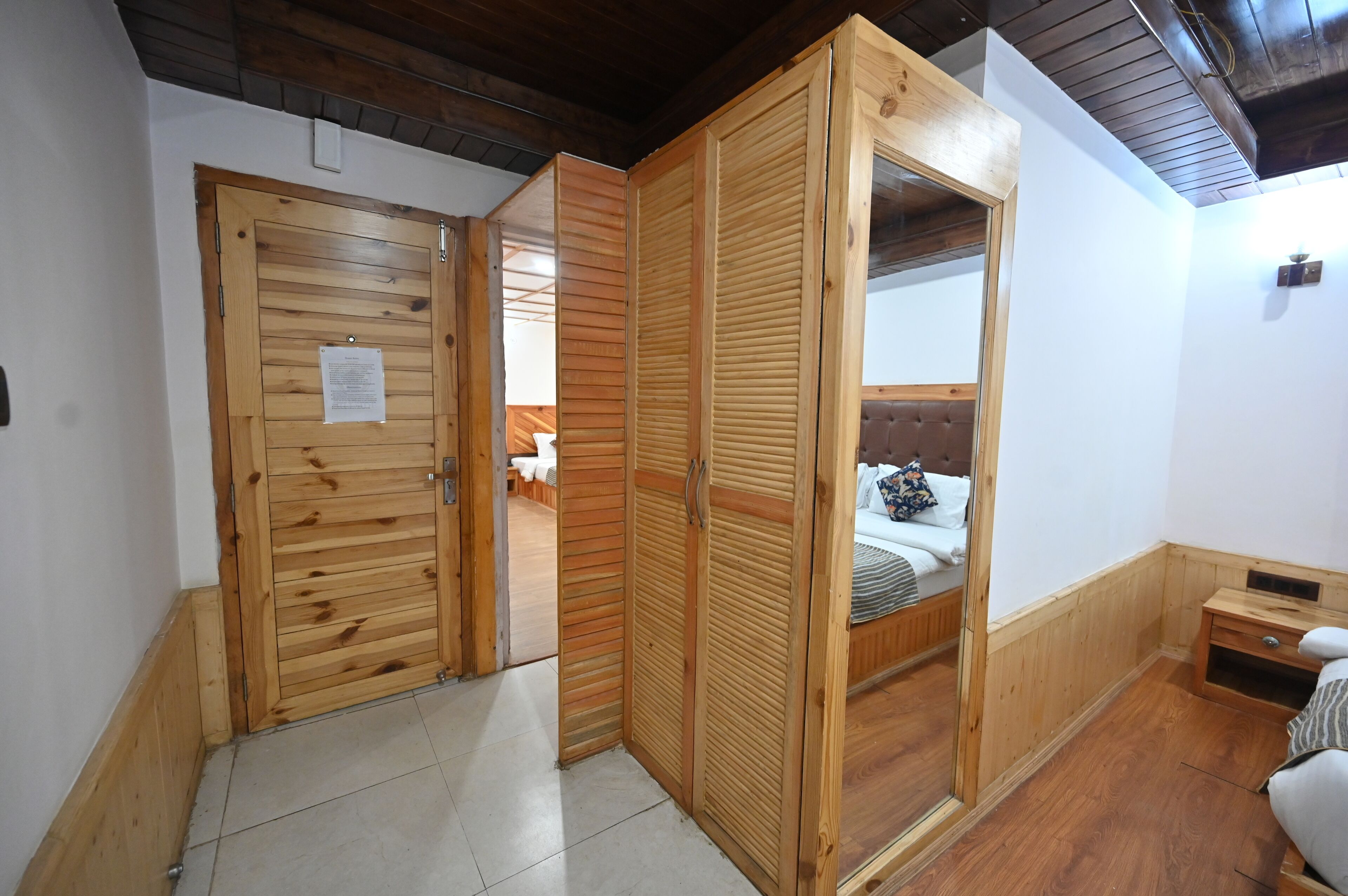A room with wooden wardrobes, a bed with a headboard, and a small bedside table.