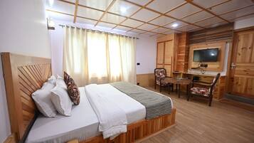 A bedroom with a wooden headboard, a bed with white linens, a bedside table with a remote control, a small desk with a chair, and a television mounted on the wall.
