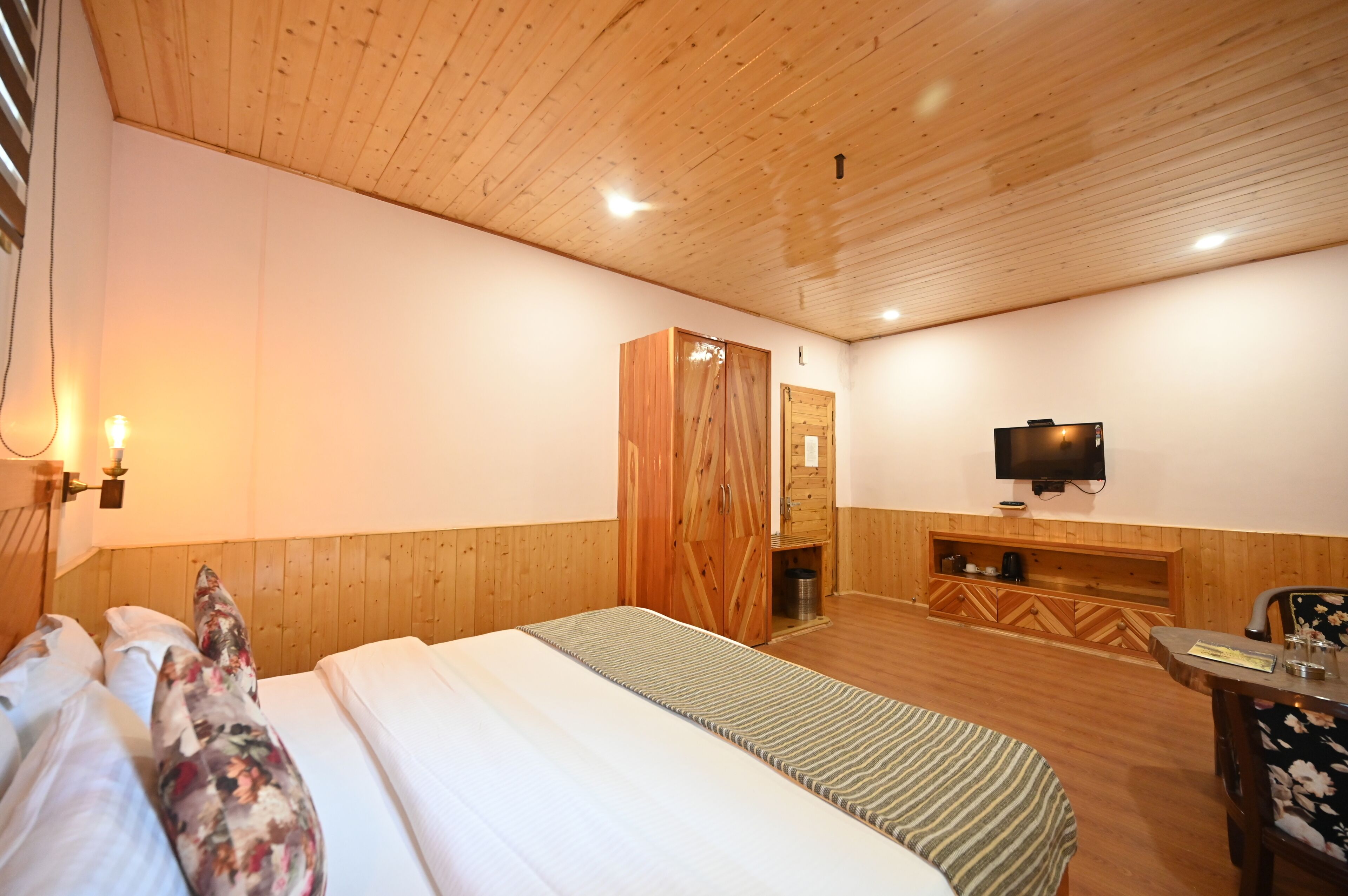 A bedroom with a wooden ceiling, a bed with floral pillows, a television, and a wooden cabinet.