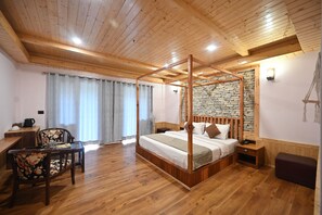 A wooden four-poster bed with a stone wall backdrop, a dining table with chairs, and a small bedside table.