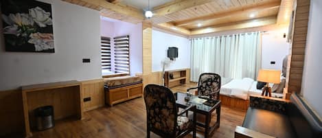 A cozy room with wooden floors, a sofa, a dining table with chairs, a bed with a nightstand, and a ceiling fan.