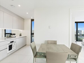A modern kitchen with white cabinets, a dining table with chairs, and a view through a window. - B-905 (Cupecoy)
