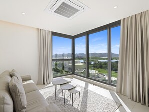 A modern living room with a large window, a sofa, and a small table. - B-905 (Cupecoy)