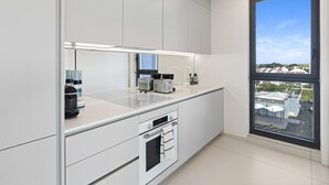 Et moderne køkken med hvide skabe, en indbygget ovn, en vask og et vindue med udsigt til bygninger.