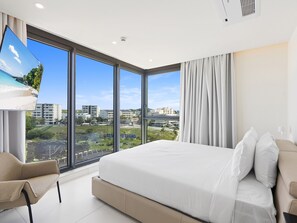 A modern hotel room with a large bed, a TV, and a view of a cityscape. - B-905 (Cupecoy)