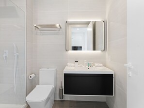 A modern bathroom with a glass shower enclosure, a white toilet, a black vanity, and a mirror above the sink. - B-905 (Cupecoy)