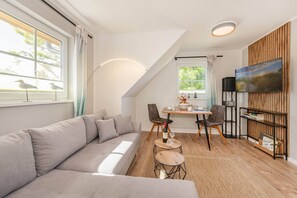 Een moderne woonkamer met een bank, eettafel, stoelen en een aan een houten wand bevestigde televisie.
