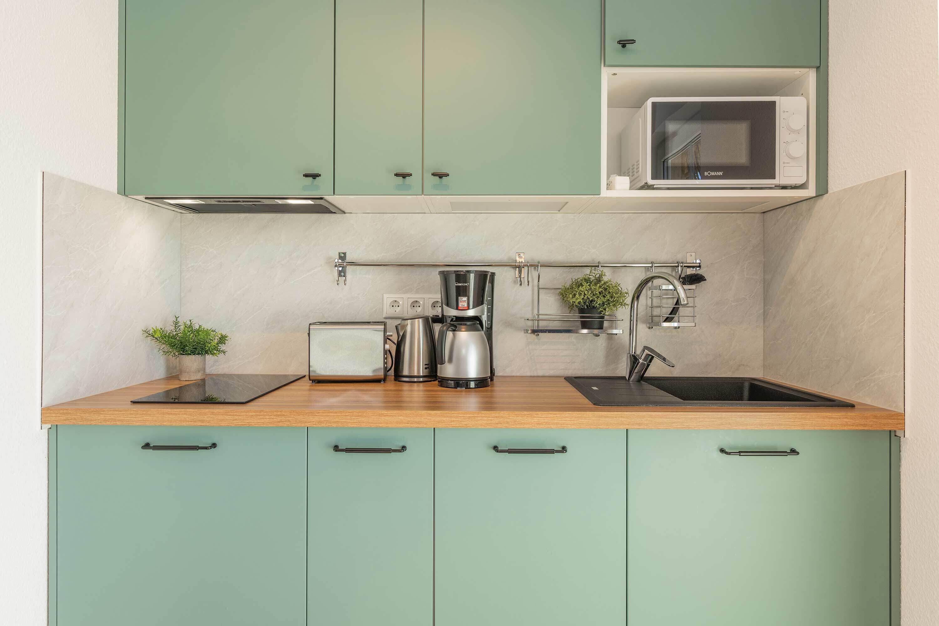 A kitchen with teal cabinets, a microwave, a toaster, a kettle, and a sink.