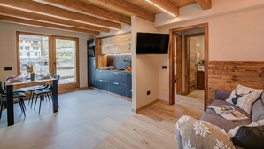 A modern interior with a dining area, kitchen, and living space, featuring wooden beams, large windows, and a flat-screen TV. - Belfiore (Livigno)