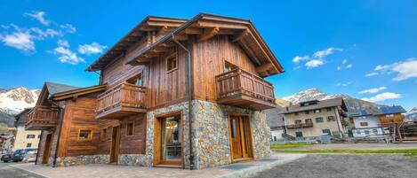 A wooden house with a stone foundation, wooden balconies, and a mountain backdrop.