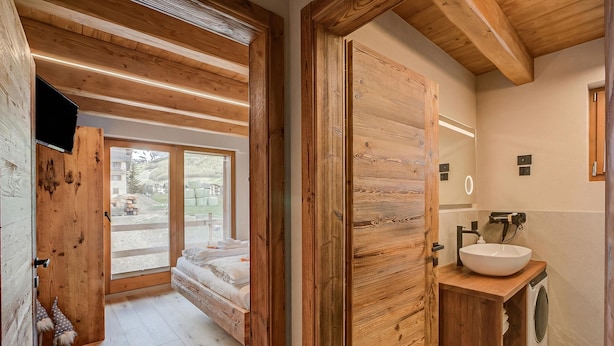 A wooden interior with a bed, a wooden cabinet with a sink, and a large window. - Belfiore (Livigno)