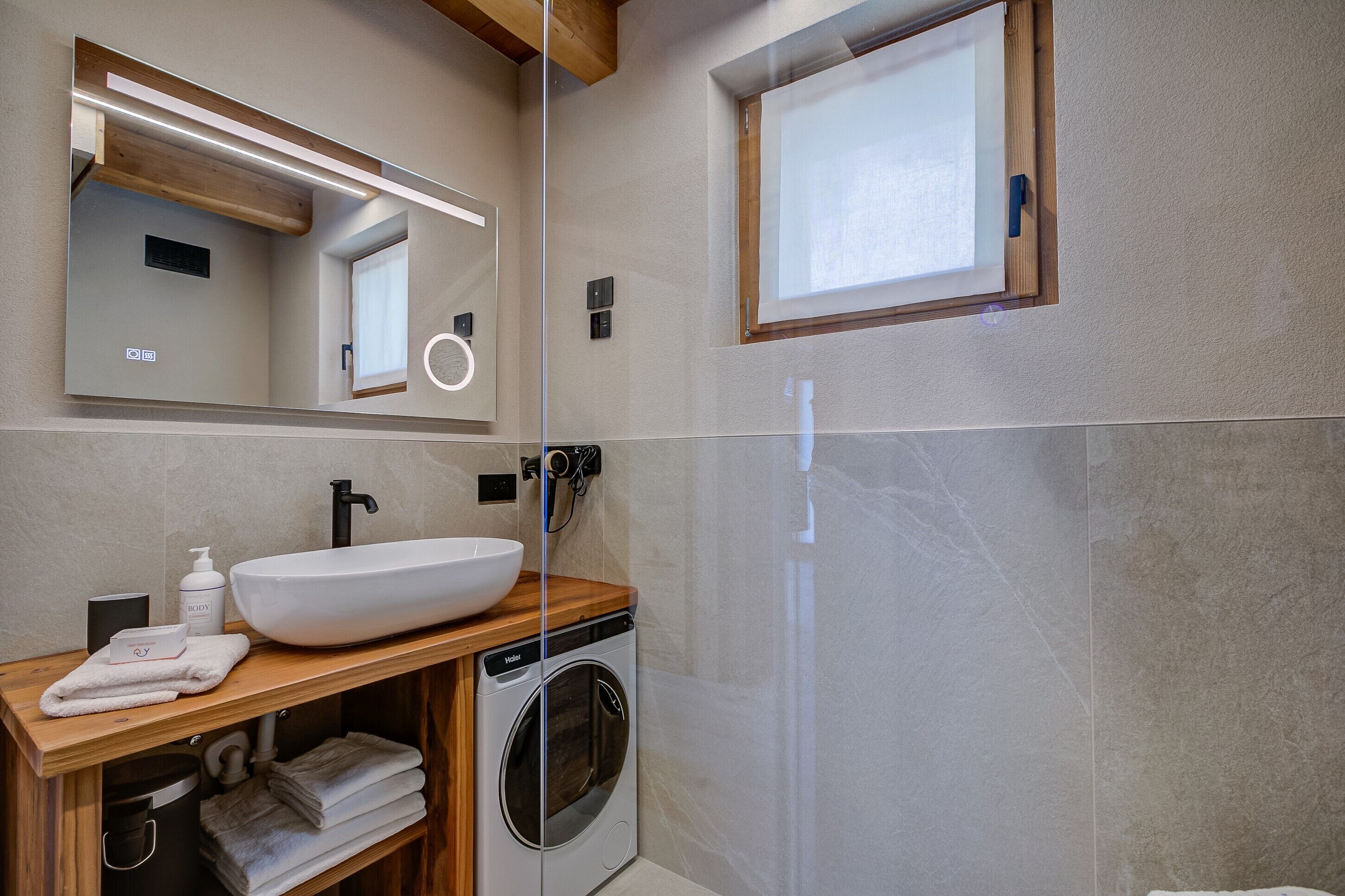 Ein modernes Badezimmer mit Waschtisch aus Holz, einer großen Spüle, einer Waschmaschine, einem Spiegel und einem Fenster.