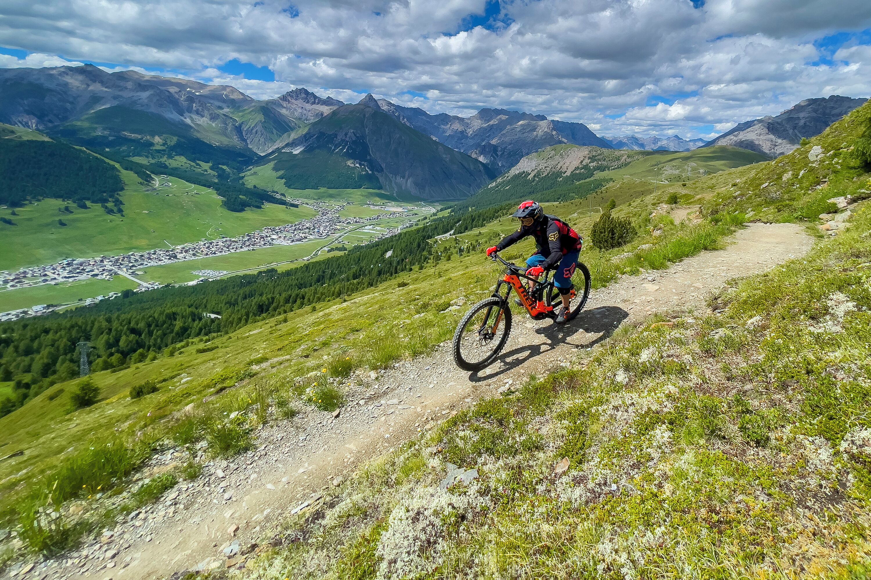 A mountain biker on a dirt trail with a view of a valley and mountains in the background.