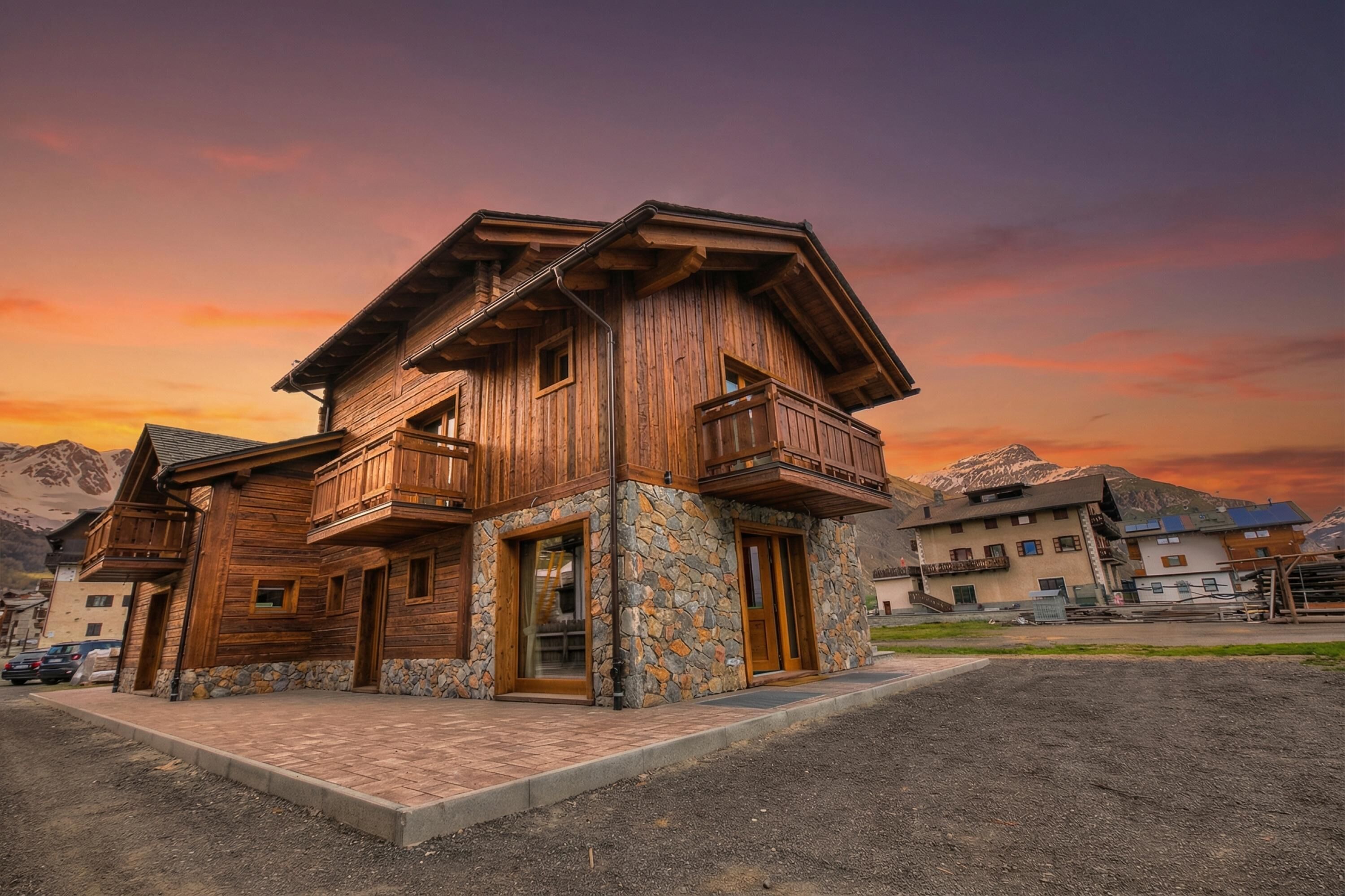 A wooden house with a stone foundation, wooden balconies, and a mountain backdrop.