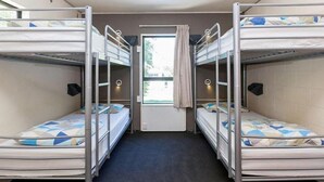 A dormitory room with bunk beds, a window with curtains, and a door.