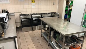 A commercial kitchen with stainless steel appliances, including multiple gas stoves and ovens, and a metal counter with various kitchen tools and containers.