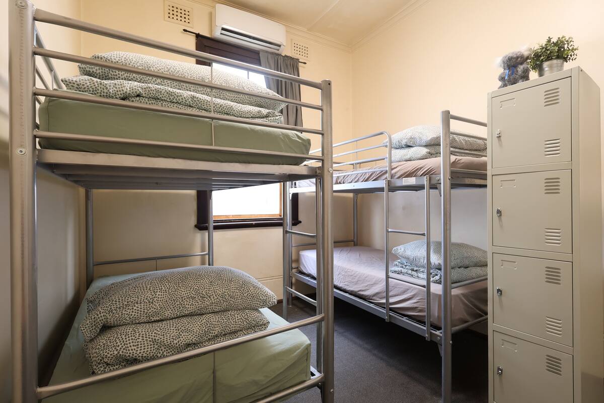 A dormitory room with bunk beds, a window, an air conditioning unit, and a set of lockers.