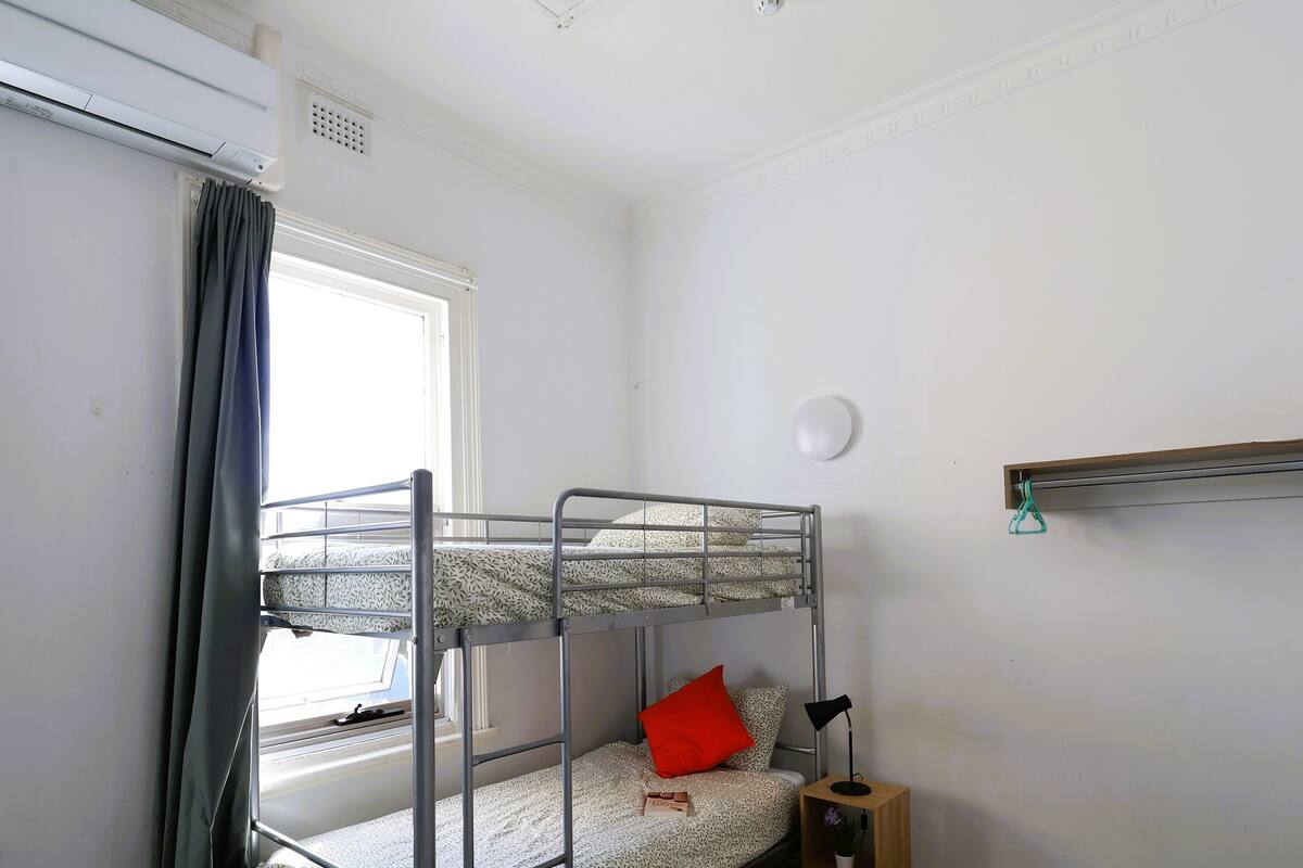 A bunk bed room with a window, a small bedside table, and a shelf.