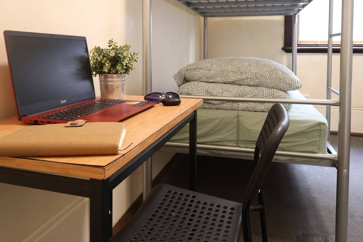 A bunk bed with a laptop and a chair in a room with a window and an air conditioner.