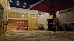 An outdoor patio area with stone walls, a wooden table and chairs, a red umbrella, and string lights. - Casa en la Montaña Cerca de la Playa (Barcelona)