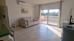 A living room with a sofa, a dining table, and a balcony with a view. - Casa en la Montaña Cerca de la Playa (Barcelona)