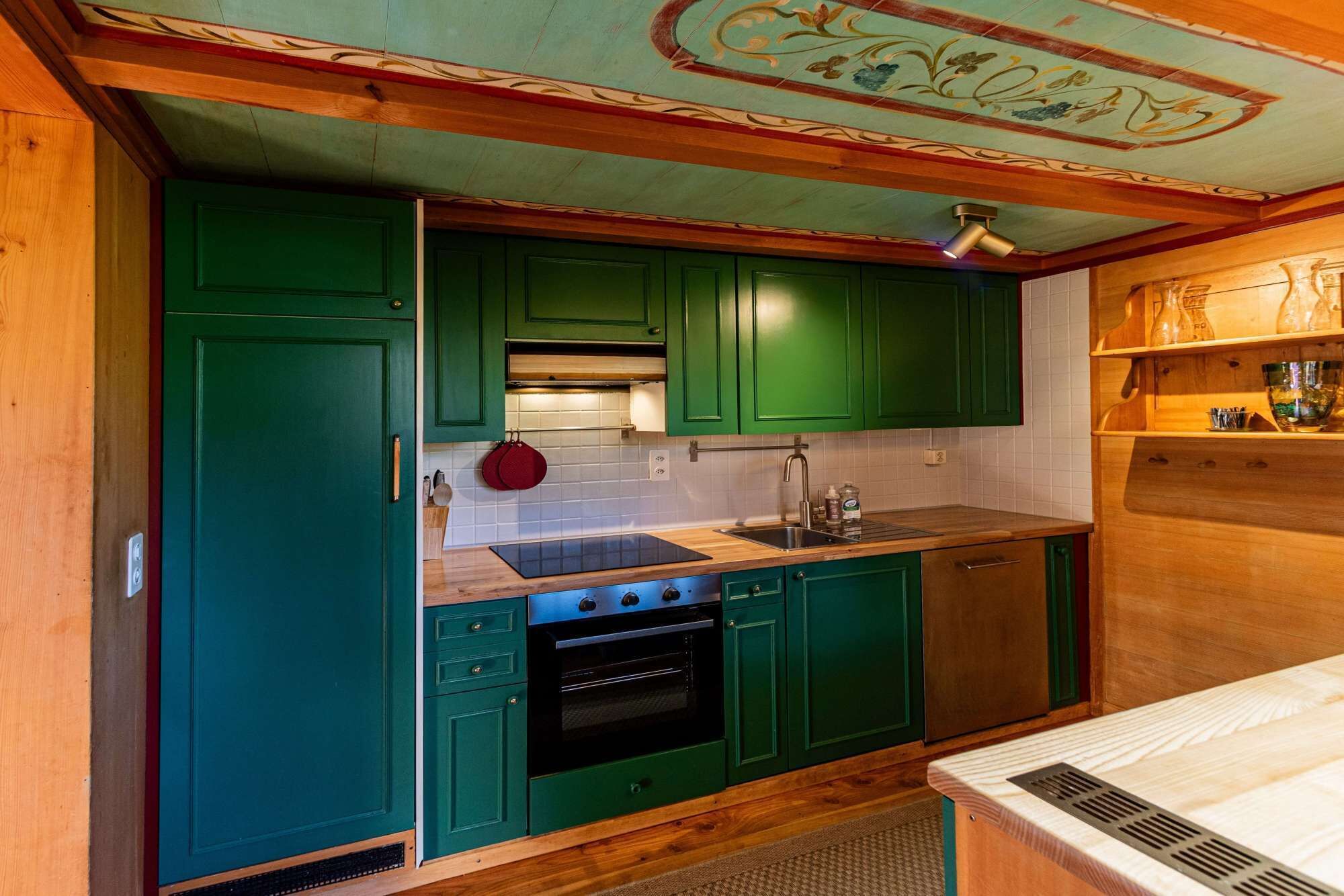 A kitchen with green cabinets, a black oven, and a wooden countertop.