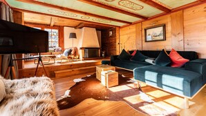 A cozy cabin interior with wooden walls, a blue sofa, a television, and a fireplace.