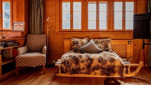 A cozy cabin interior with a wooden bed, a patterned armchair, and a bookshelf.