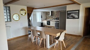A modern kitchen with a stone wall, wooden beams, and a dining area with a wooden table and chairs.