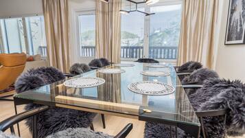 A modern meeting room with a glass table, multiple chairs, and a view of a balcony with blinds.