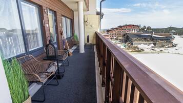 A balcony with wicker furniture, a view of a building with a ski lift, and a snowy landscape.