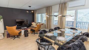 A modern living room with a glass dining table, leather chairs, a sofa, and a flat-screen TV.