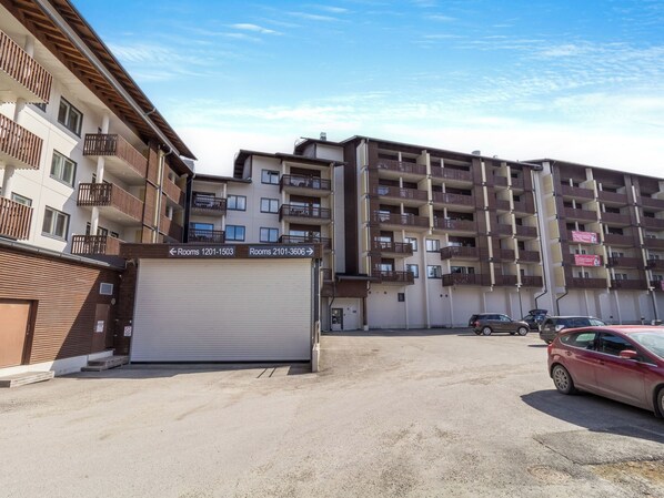 A multi-story residential building with balconies and a parking area.
