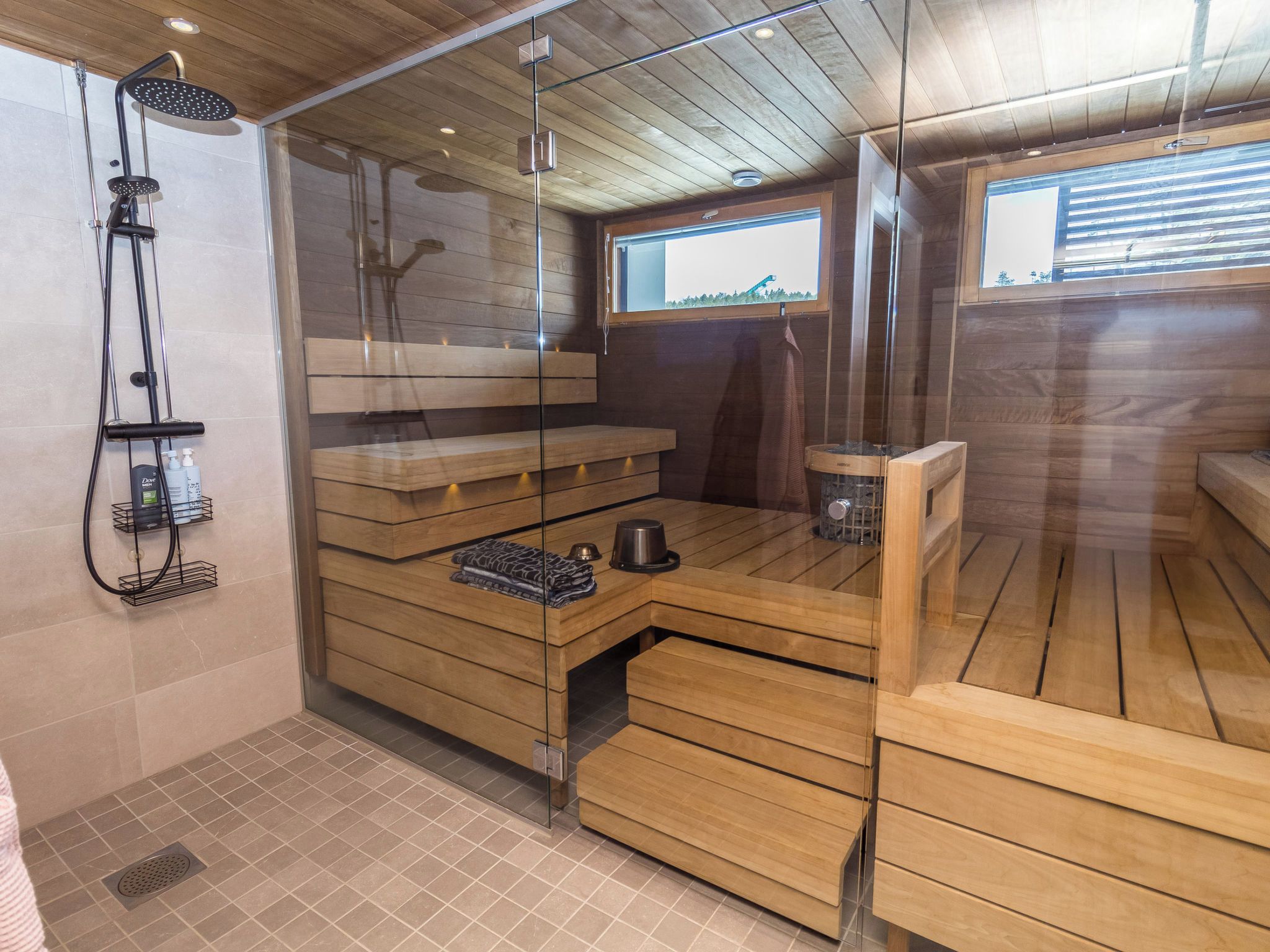 A sauna room with wooden benches, a glass partition, and a shower area with a handheld showerhead.