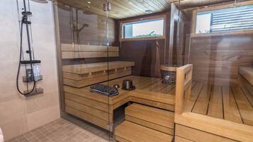 A sauna room with wooden benches, a glass partition, and a shower area with a handheld showerhead.