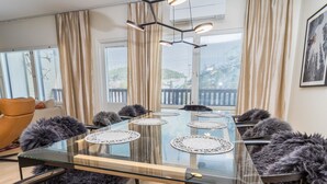 Ett modernt matrum med ett glasbord, svarta stolar med fällbara fällar och utsikt genom stora fönster med persienner.