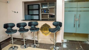 A bar area with four black bar stools, a minibar with bottles, and a wooden counter with a logo. - Everland Hotel and Suites (Ojodu Berger)