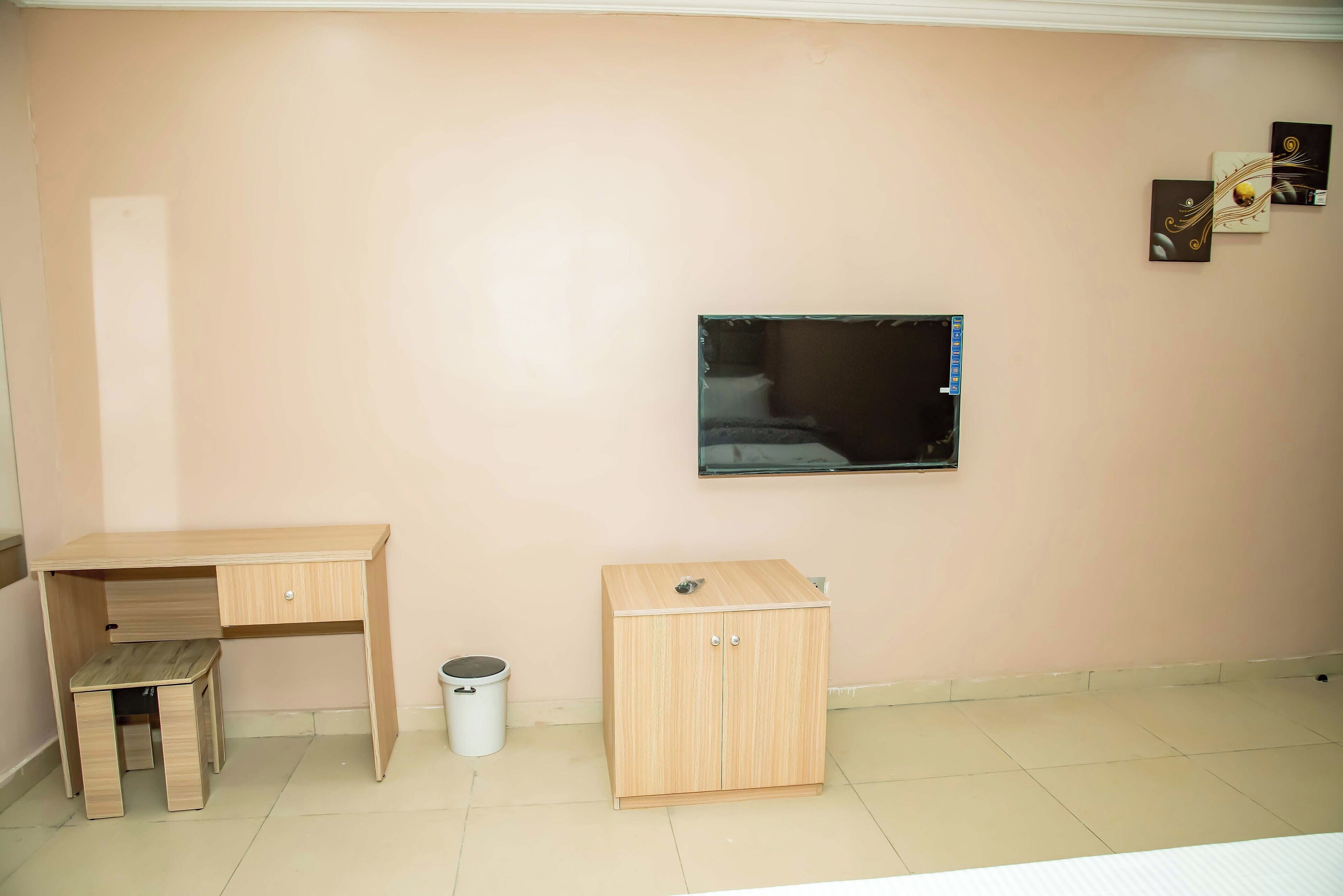 Una habitación con un escritorio, un archivador pequeño, un cesto de basura y un televisor de pared.