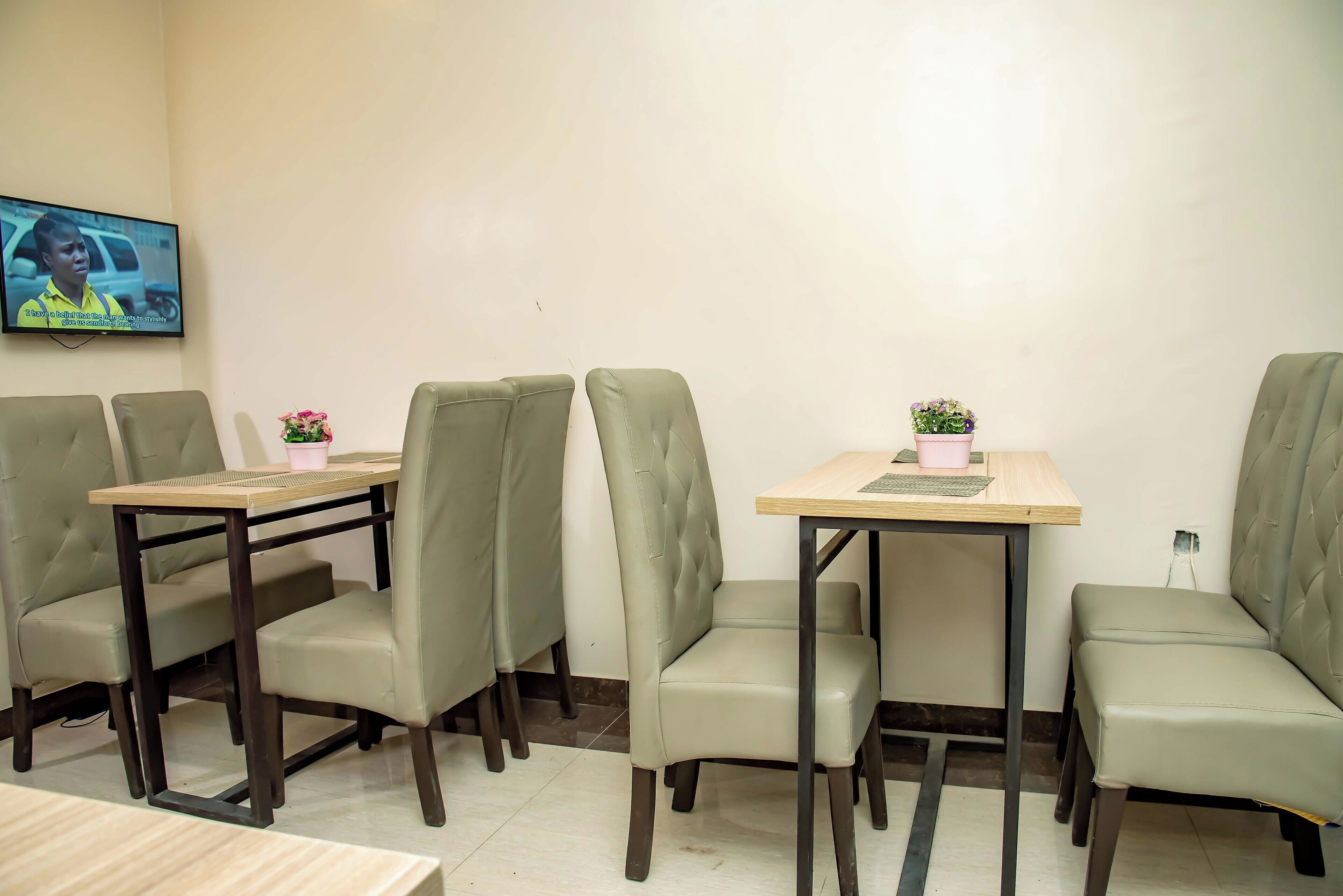 A dining area with four tables and chairs, a television mounted on the wall, and a small potted plant on one table.