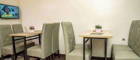 A dining area with four tables and chairs, a television mounted on the wall, and a small potted plant on one table.