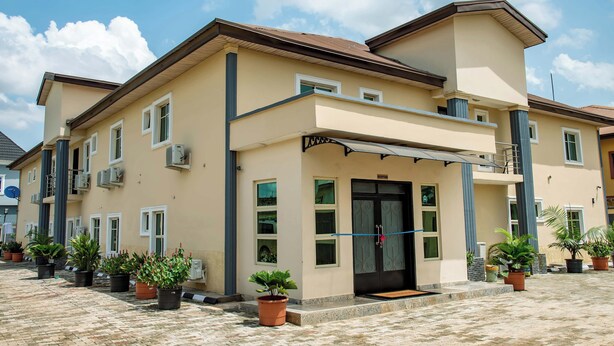 A two-story building with a beige facade, multiple windows, and a black front door. - Everland Hotel and Suites (Ojodu Berger)