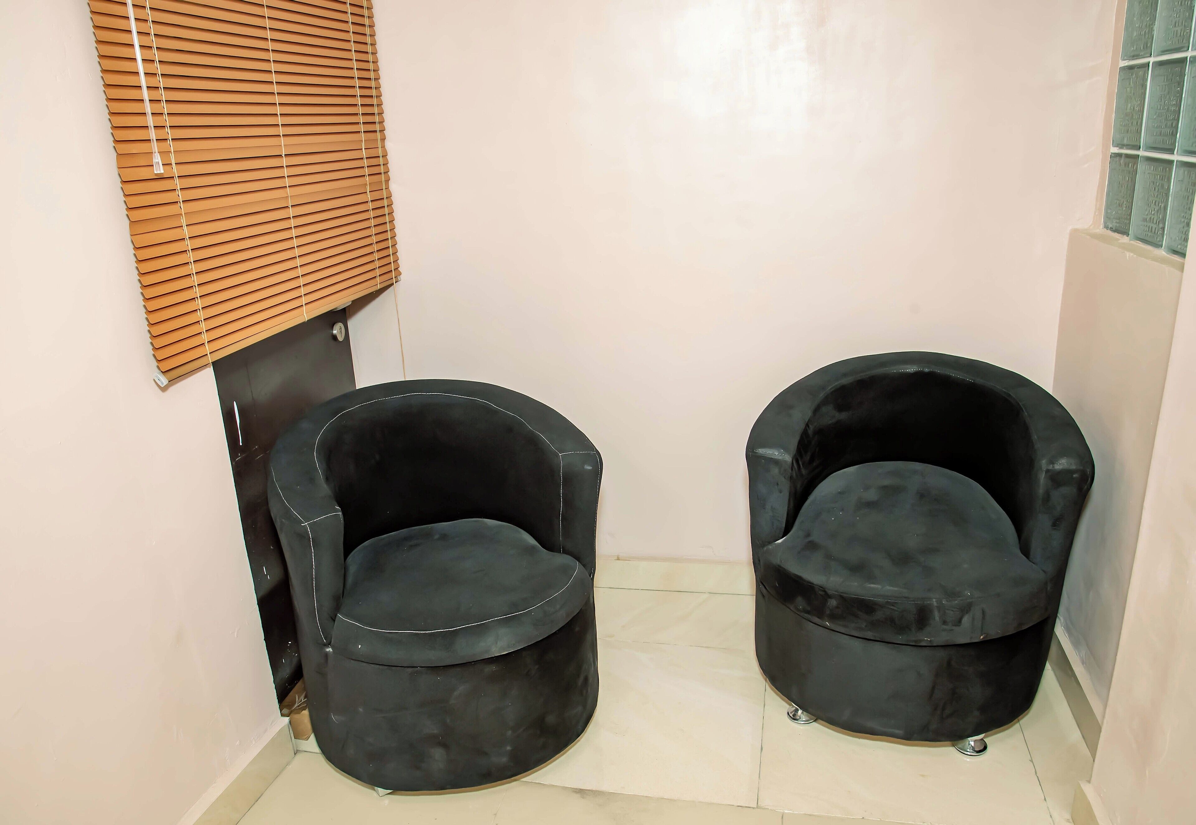 Dos sillones negros en un rincón junto a una ventana con persianas.