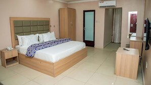 A hotel room with a large bed, a wardrobe, an air conditioning unit, a bedside table, and a small desk. - Everland Hotel and Suites (Ojodu Berger)