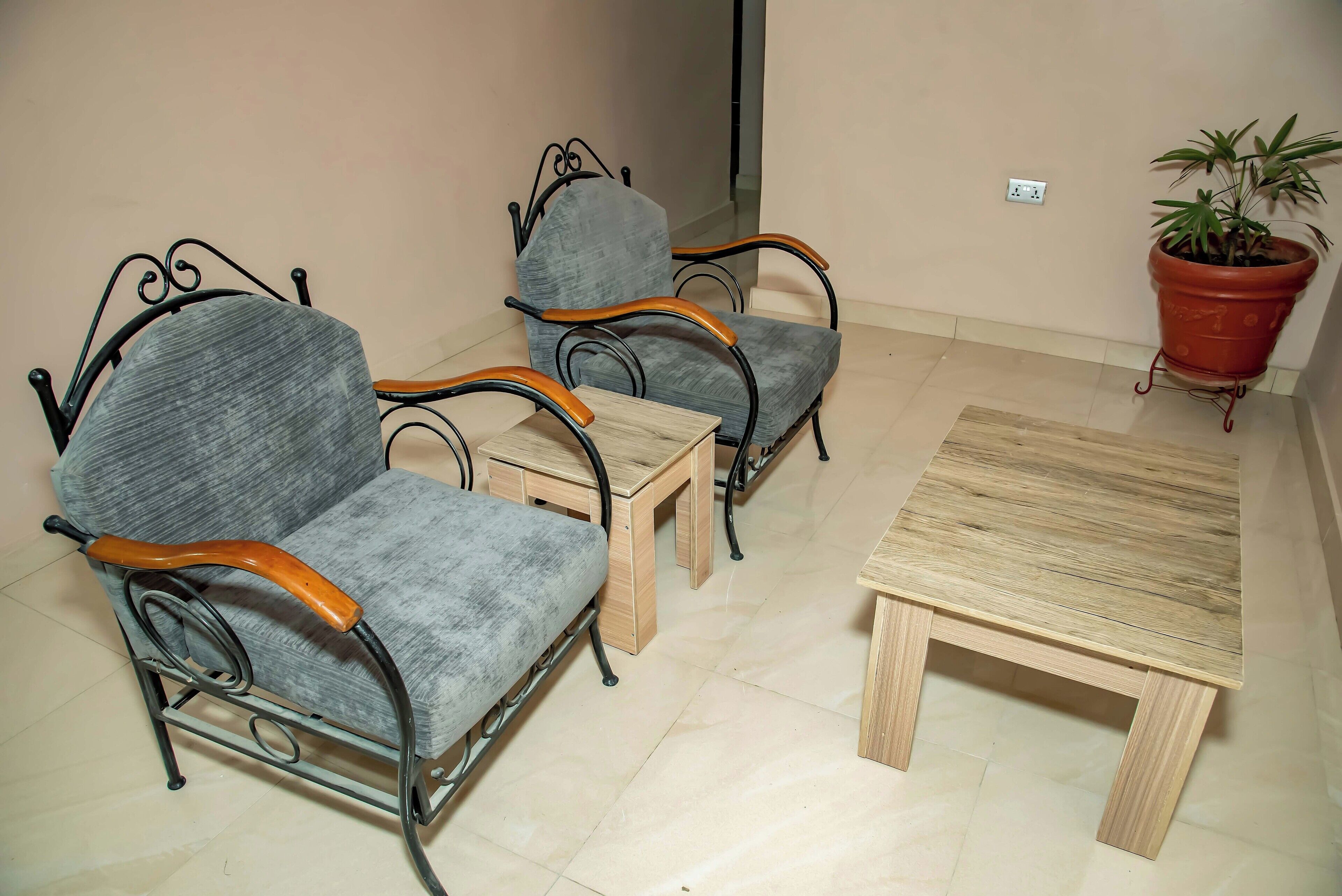 A room with two grey upholstered chairs with wooden armrests and metal frames, a small wooden table, and a potted plant.